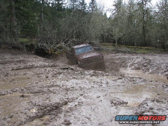 Truck stuck in deep mud, tires churning up water and muck
