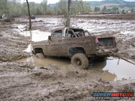Mud-covered pickup truck stuck in mud, with other vehicles in background