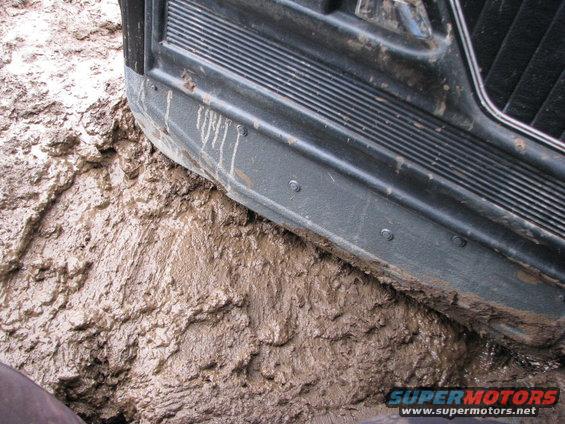 Close-up of a vehicle's side panel and running board deep in thick mud