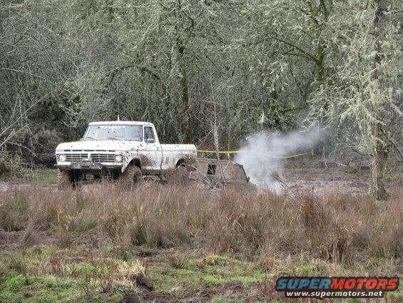 White pickup truck stuck in mud, emitting smoke from exhaust