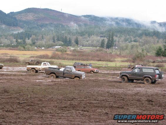 Several trucks and SUVs stuck in mud, with a mountain and trees in the background