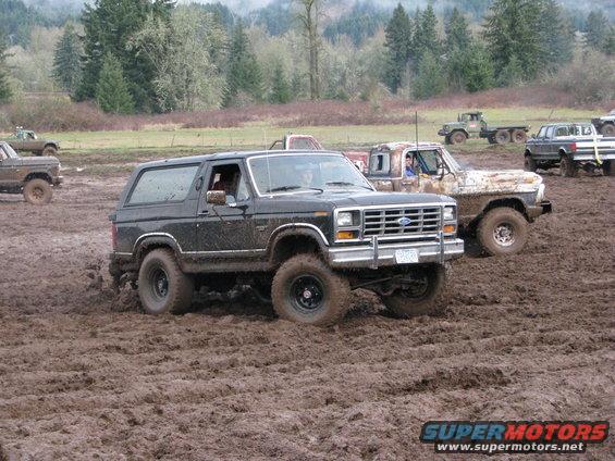 Black Ford Bronco with lifted suspension driving through mud, front grille visible