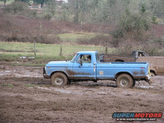 Blue pickup truck stuck in mud, side view. Another truck is behind it