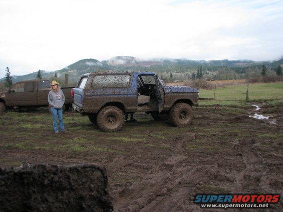 Mud-covered blue 1978 Ford Bronco parked in a muddy field with a person standing nearby