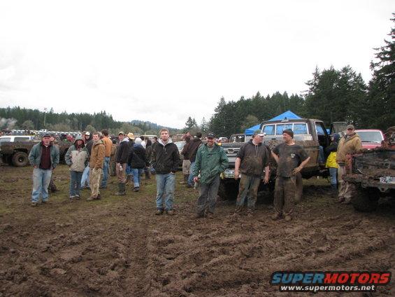 Group of people standing around muddy trucks and SUVs in a field