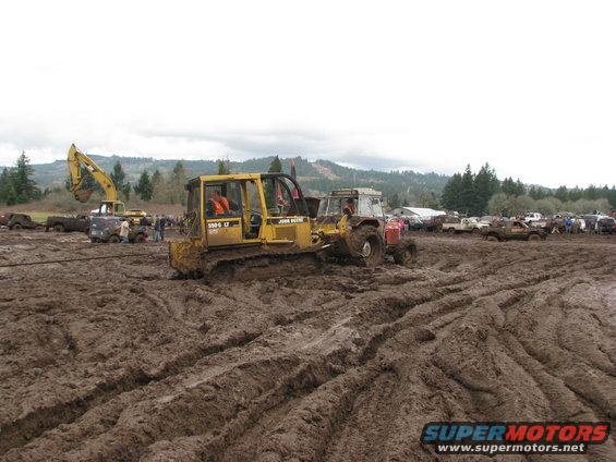 John Deere bulldozer and tractor stuck in mud, with other vehicles in background