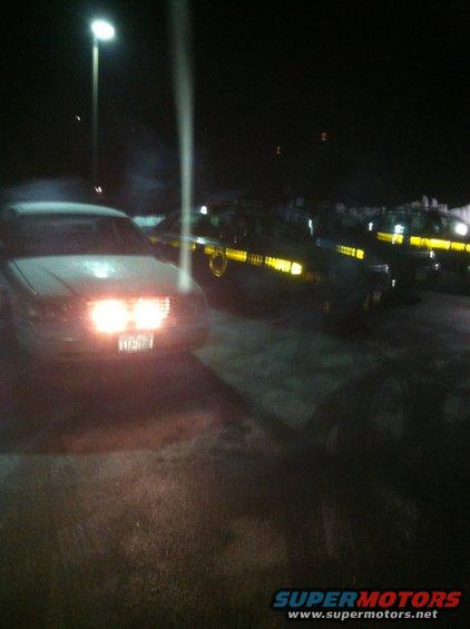 Front view of a 2000 Ford Crown Victoria with headlights on, parked at night next to other police cars