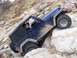 2004 Jeep Wrangler - A blue Jeep Wrangler navigates a challenging rocky terrain, with two occupants inside.