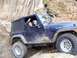 2004 Jeep Wrangler - A blue Jeep Wrangler navigates a muddy, rocky trail with a person waving from the driver's seat.