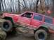 2004 Jeep Wrangler - A red Jeep Cherokee XJ navigates a rocky, muddy off-road course, demonstrating its climbing capabilities.