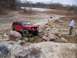 2004 Jeep Wrangler - A red Jeep Cherokee XJ is driven over large rocks in an outdoor off-road park.