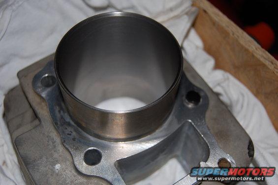 Engine cylinder with metal casing and mounting holes, resting on white cloth