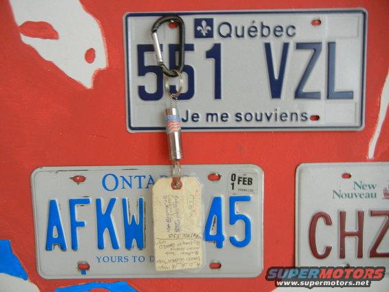 License plates from Quebec and Ontario hang on a red wall with a keychain