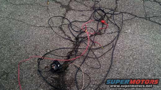 Tangled black and red electrical wires with a small black box on cracked asphalt