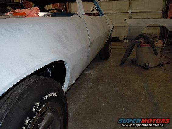 Car body in primer, 3/4 front view, showing fender and door. Tires have white lettering
