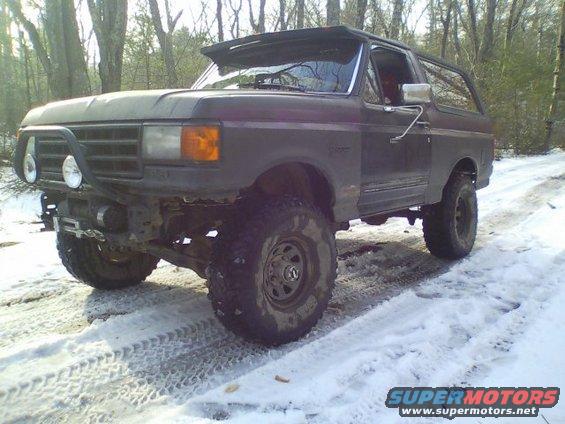 Dark gray Ford Bronco with off-road tires and a brush guard on a snowy dirt road
