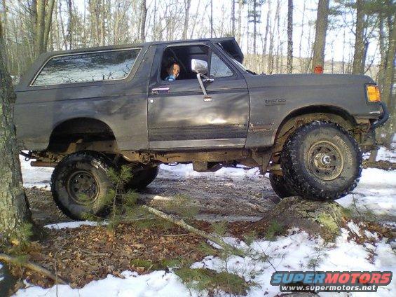 Dark gray 1989 Ford Bronco off-roading over rocks and snow