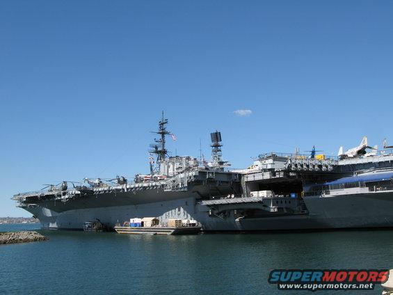 aircraft carrier docked in harbor with helicopters on deck