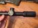 1996 Ford Bronco - A rifle scope is held in a hand, with a logo visible on its side.