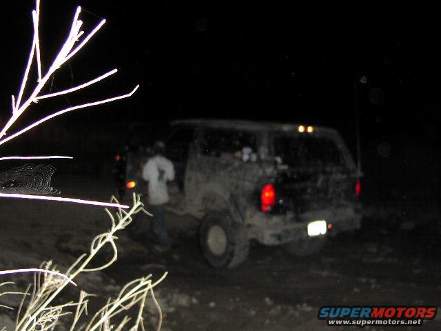 Mud-covered SUV at night, rear view. Red taillights visible