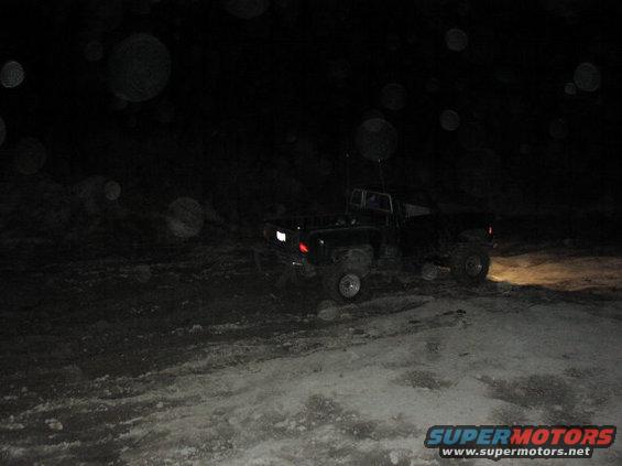 Pickup truck with headlights on, driving on a snowy or muddy path at night