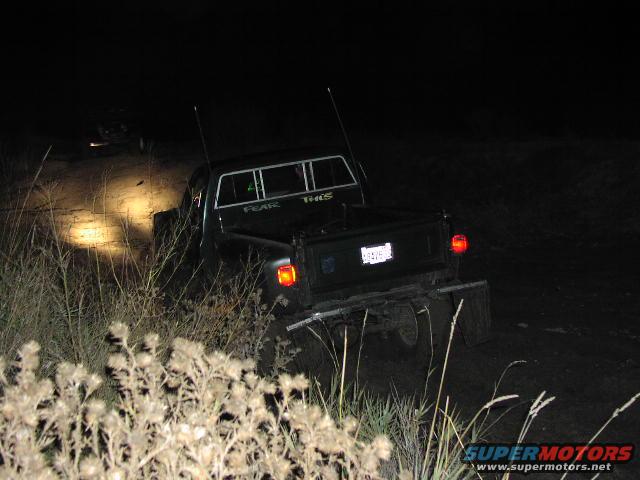 Pickup truck driving off-road at night, another vehicle in distance. Text on back window says 'FEAR THIS'