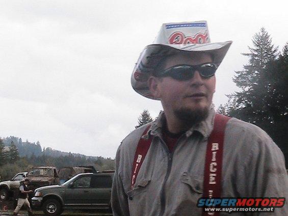 Man wearing a cowboy hat and red suspenders, with several trucks parked behind him in an outdoor setting