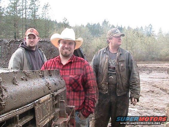three men standing in mud, one wearing a cowboy hat