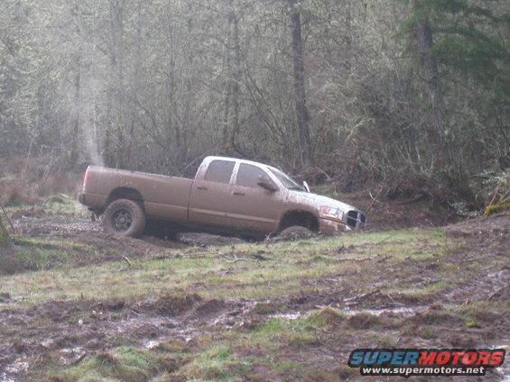 Pickup truck stuck in muddy terrain with trees in background