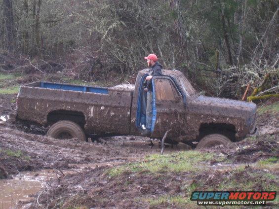 guy in red hat leaning out of a mud-caked pickup truck stuck in a muddy ditch