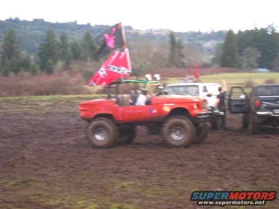 Red off-road vehicle with large tires and a flag flying in a muddy field