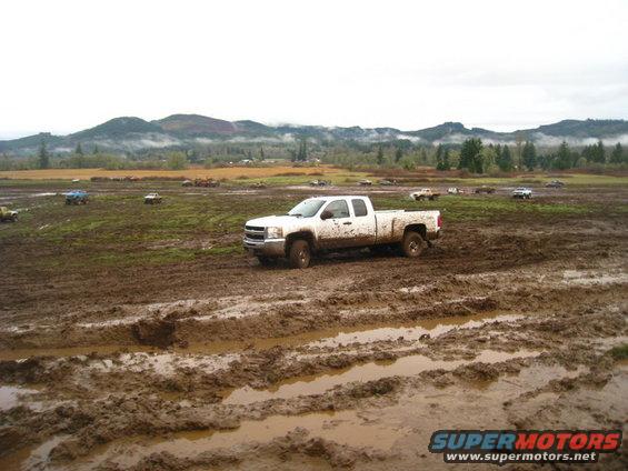 White pickup truck in a muddy field with other vehicles in the background