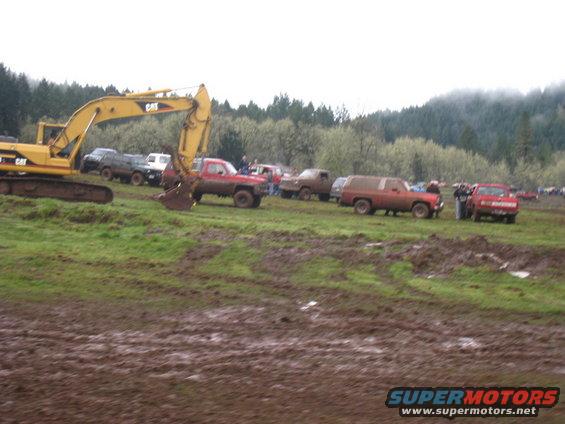 Muddy field with excavator and multiple trucks parked in the background