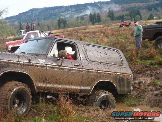 Mud-covered 1978 Ford Bronco stuck in mud with driver wearing a cowboy hat