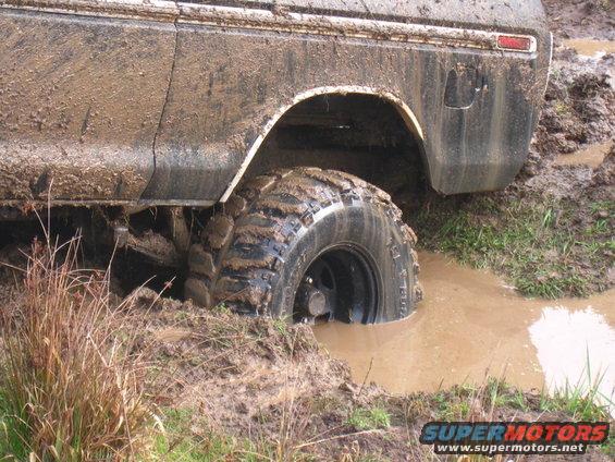 Muddy off-road vehicle with large tires stuck in a muddy puddle
