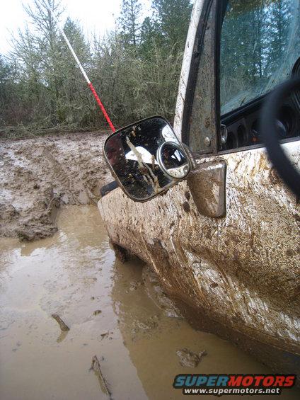 Mud-splattered side mirror and door of an off-road vehicle stuck in mud