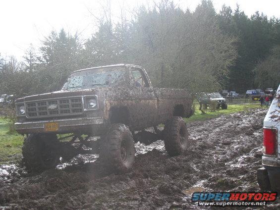 Mud-covered pickup truck with lifted suspension driving through mud