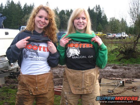 Two women in overalls showing Hooters t-shirts, one from Warner Robins, GA, the other from Macon, GA