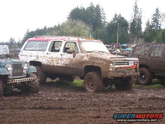 Muddy SUV and Jeep in a muddy field with trees in the background