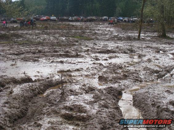 Muddy field with many off-road vehicles in the background