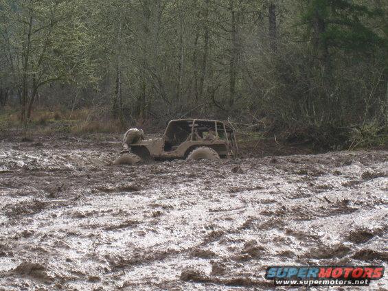Off-road vehicle stuck deep in mud, side view. Watermark 'SUPERMOTORS.NET'