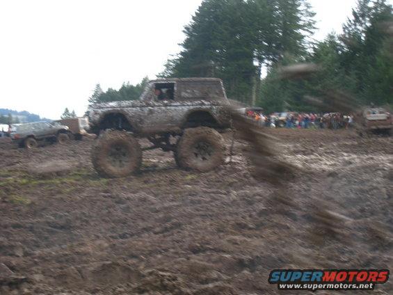 muddy off-road truck with big tires driving through a mud pit, crowd watching in background