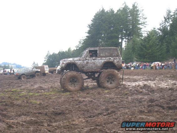 Mud-covered 1978 Ford Bronco with oversized tires in a muddy field