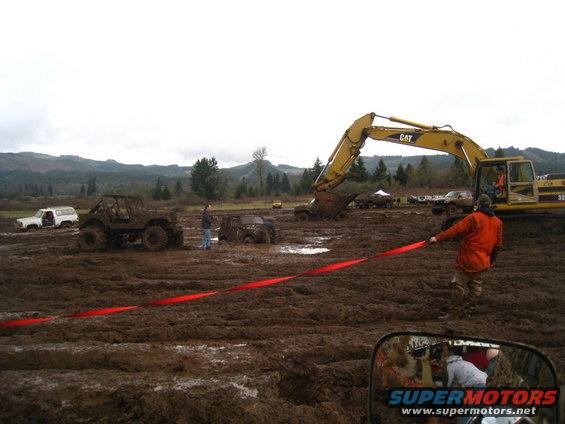 Off-road vehicles stuck in mud, excavator in background