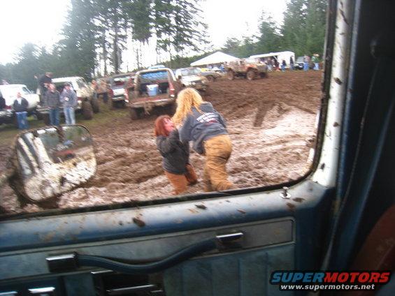 Muddy off-road vehicles stuck in mud with people around, viewed from inside a vehicle