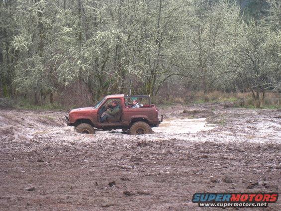 Red off-road vehicle stuck in mud with people inside