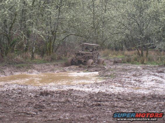 Off-road buggy driving through a muddy field with trees in the background