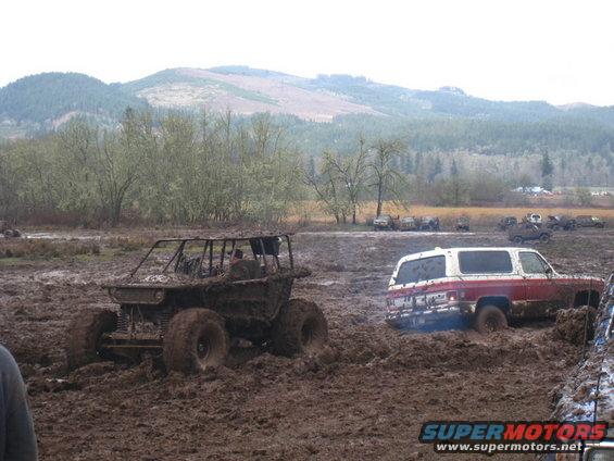 Red and white SUV stuck in mud, with a custom off-road buggy nearby