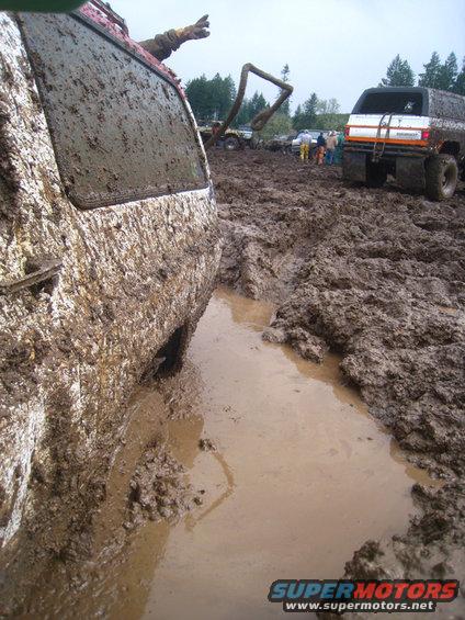 Muddy vehicles stuck in a mud pit, one with a person's arm sticking out the window