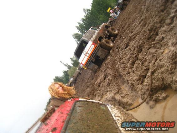 Mud bog with several off-road trucks stuck in deep mud. A red vehicle is in the foreground
